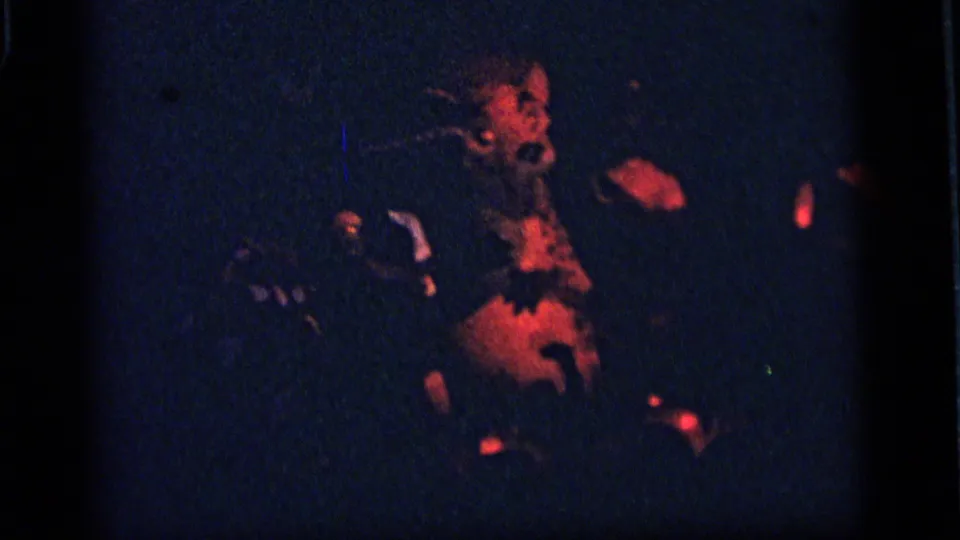 1964 Camden home-movie frame showing a dim amusement-park display with a dog-like figure and nearby shadowed visitors or figures.