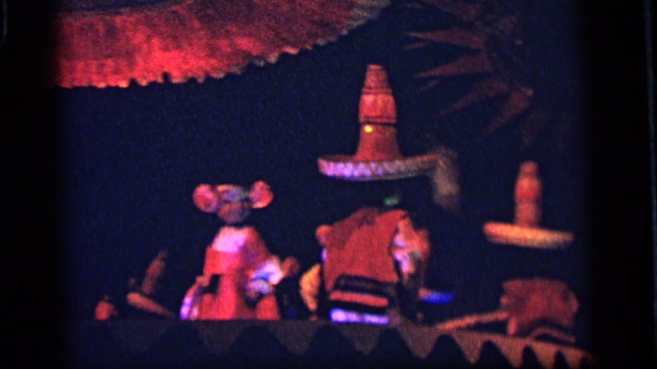 1964 Camden frame with blue and red lighting over umbrella-like canopies and small festival figures on a dark set.