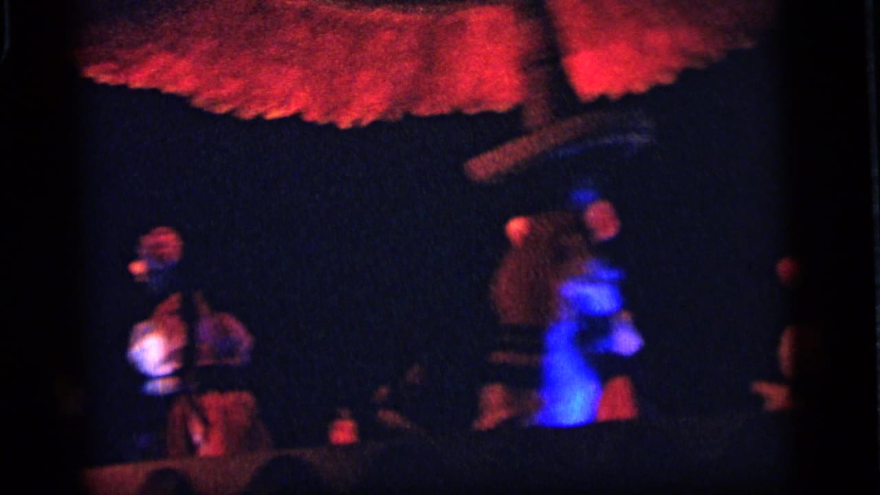 1964 Camden home-movie view of small illuminated figures under a red canopy, with strong blue spill light and soft focus.