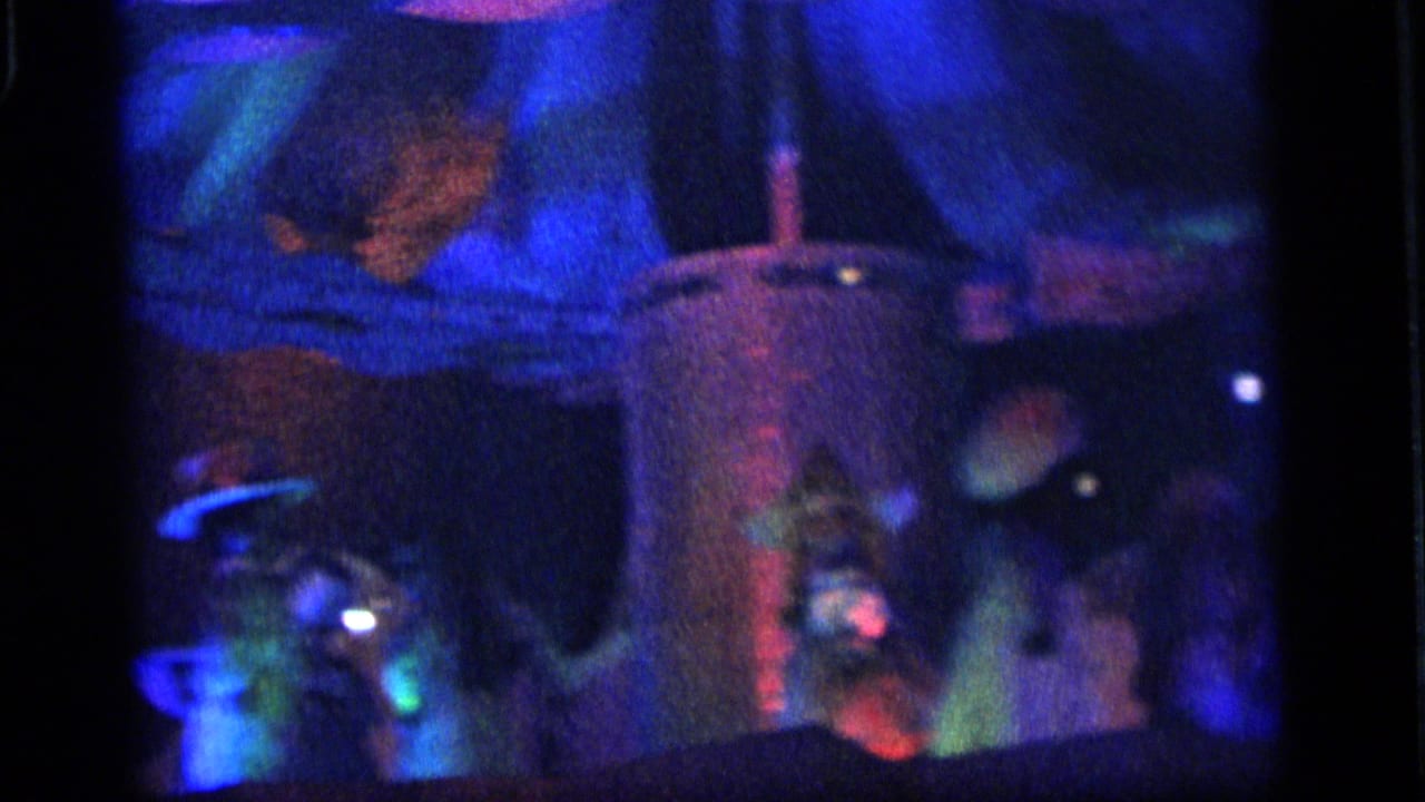 Dark carnival display with blue light, cloud-like forms, and a dim vertical illuminated structure.