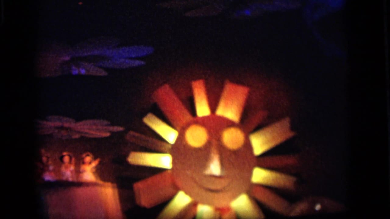 1964 Camden carnival display with a glowing sun face, colored ray panels, small figure props, and stylized cloud forms in darkness.