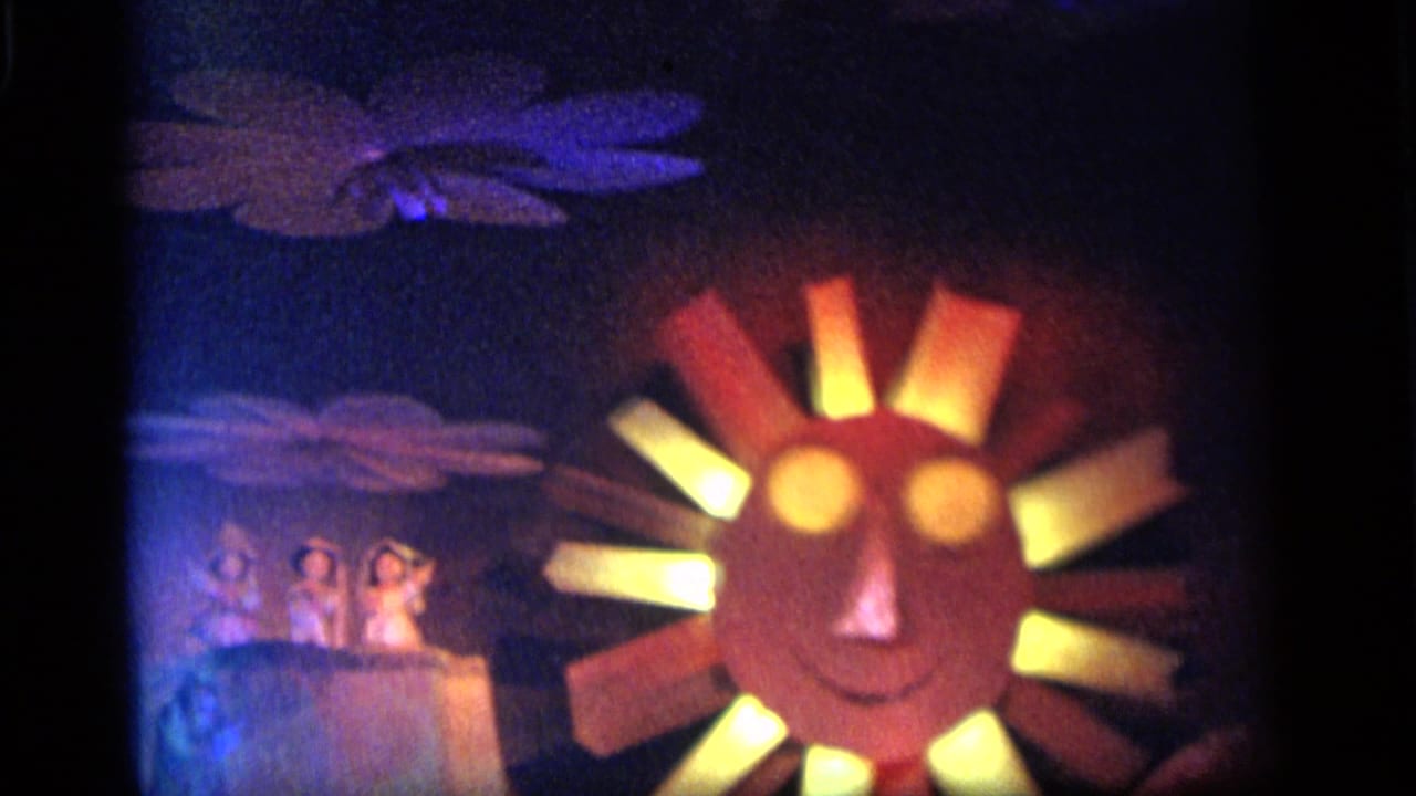 1964 Camden 8mm frame centered on a smiling sun-face carnival prop with glowing eyes, colored rays, and small figures to the side.