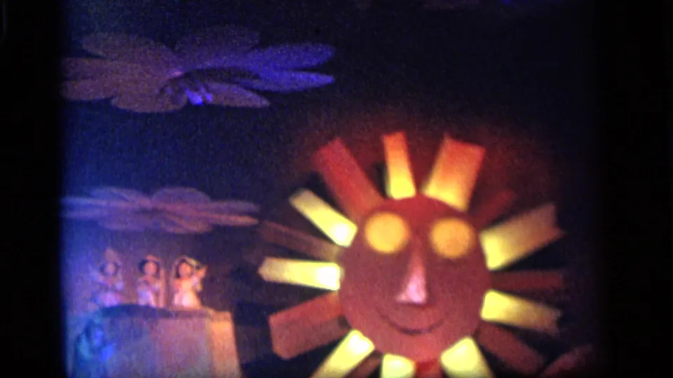 1964 Camden 8mm frame centered on a smiling sun-face carnival prop with glowing eyes, colored rays, and small figures to the side.