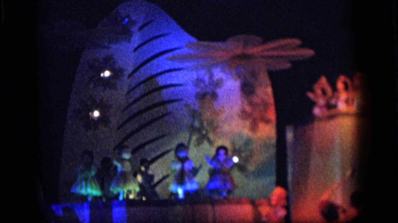 Colorful toy stage with small figures in front of a large curved backdrop.