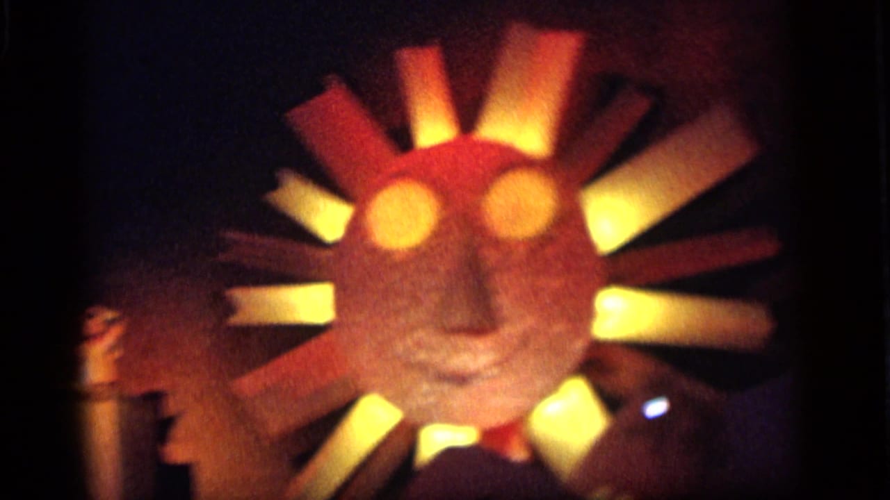 1964 Camden home-movie frame with a large illuminated sun-face stage prop and radiating yellow and red panels.