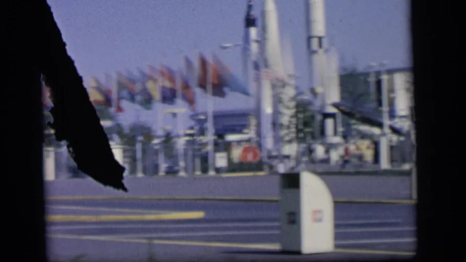 Camden, New Jersey view of flags, steps, street fixtures, and distant pedestrians near a large white structure in 1964 footage.