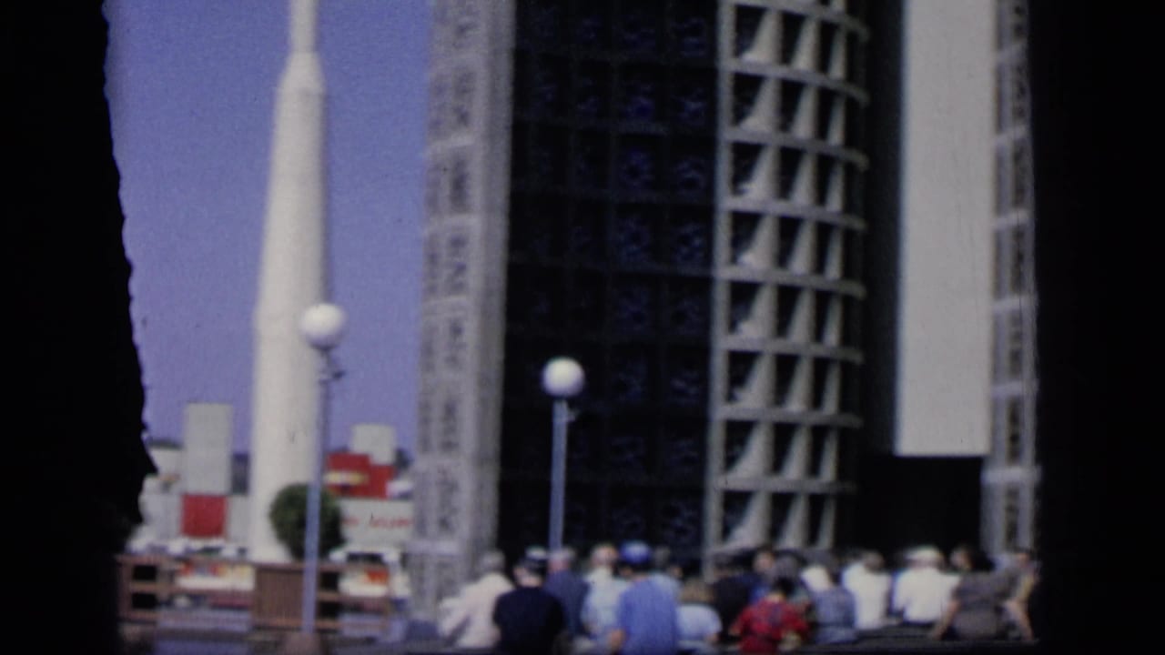 1964 Camden home-movie frame showing visitors near the base of a white geometric modern building under a blue sky.