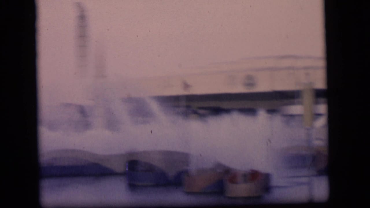 Water fountains seen through dark window frames with buildings in the background.