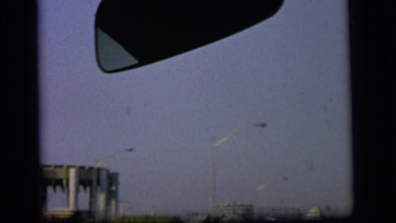 1964 Camden home-movie frame from a moving vehicle, showing industrial structures, utility poles, pale sky, and dark 8mm frame edges.