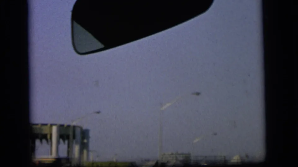 1964 Camden home-movie frame from a moving vehicle, showing industrial structures, utility poles, pale sky, and dark 8mm frame edges.