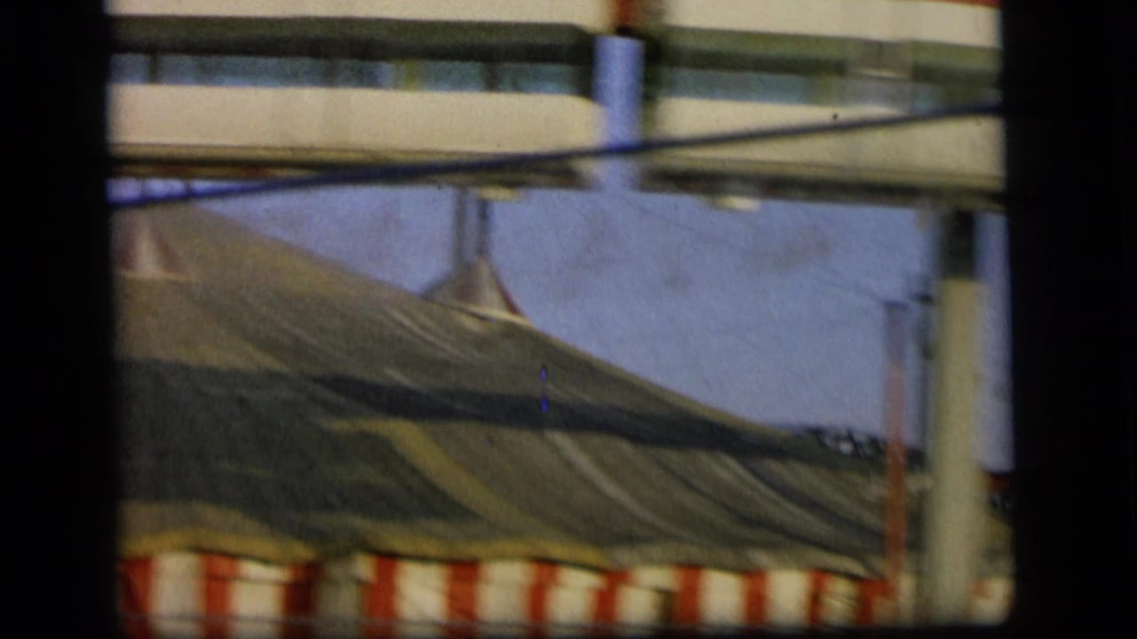 Large tent canopy with red-and-white striped trim beside concrete overhead structures.