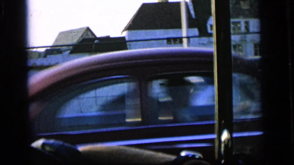 1964 Camden street view from inside a moving car, with a red car and roadside buildings beyond the window.