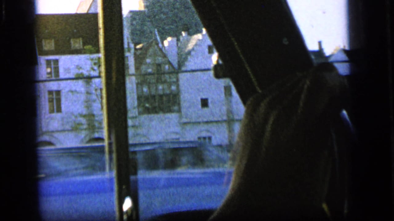 Vehicle interior framing a white building outside, with a hand or arm at the right edge.