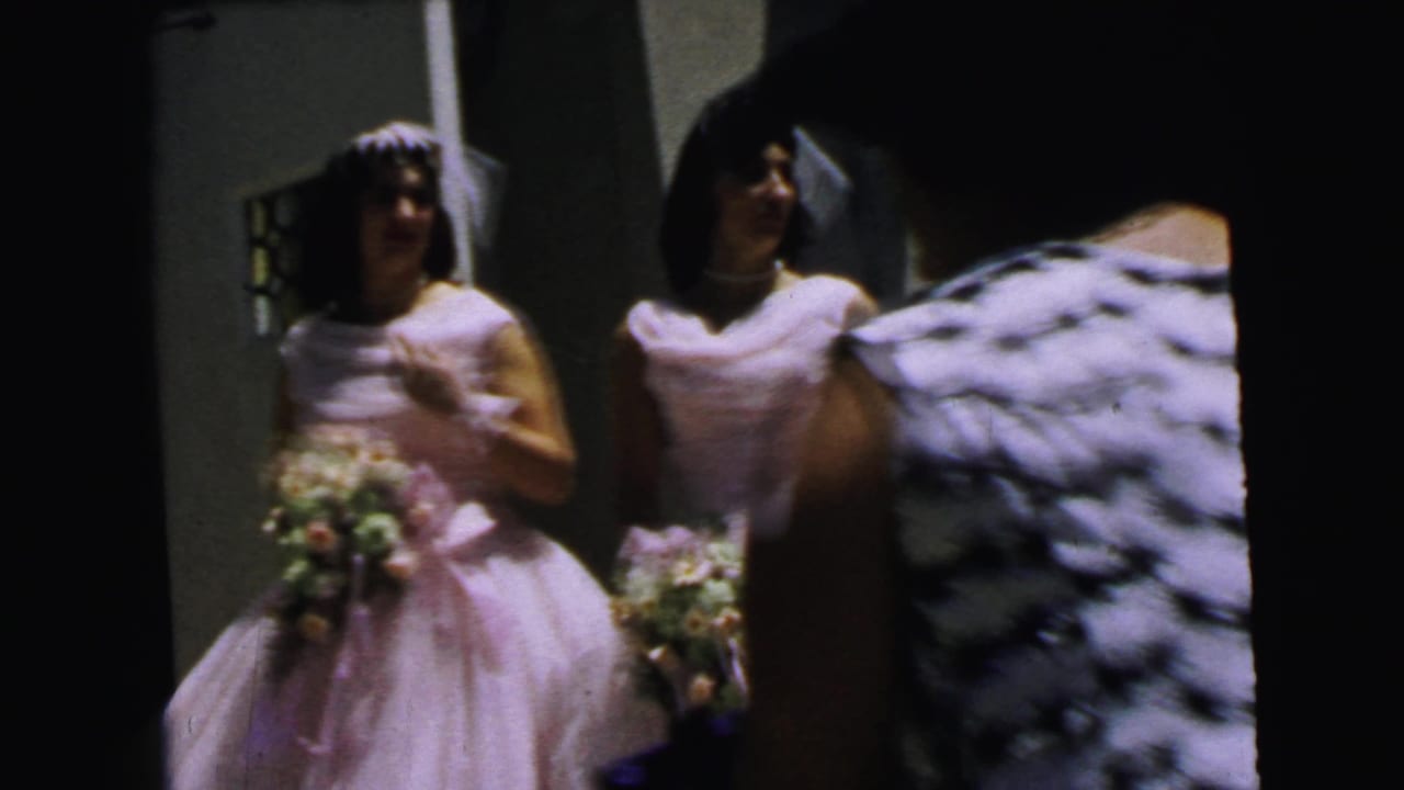 1964 Camden home-movie frame showing a bride and bridesmaids with veils and bouquets outside a building entrance.