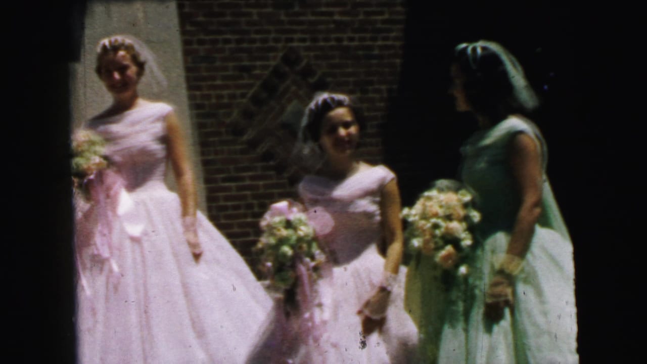 Bridesmaids in pink and green dresses stand outside a brick building holding bouquets.