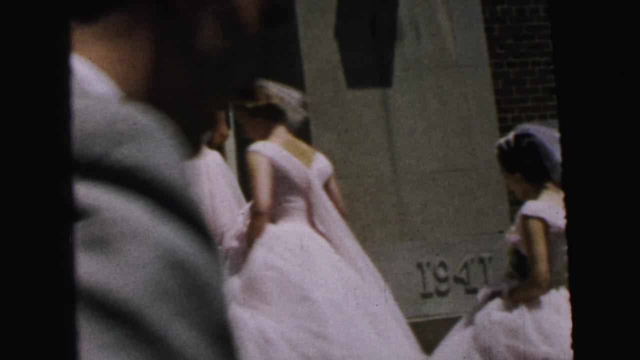 1964 Camden 8mm frame showing bridesmaids in white dresses entering a church doorway, partly obscured by a close foreground figure.