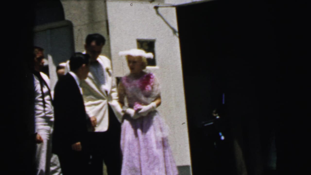 1964 Camden church exterior with a woman in a lavender dress and white hat beside men in formal wear, seen in bright sun.
