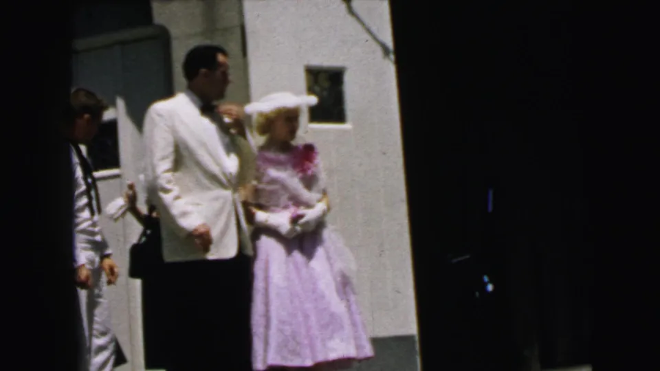 1964 Camden frame showing the formal couple by a plain wall, with the sailor partly visible at the edge.