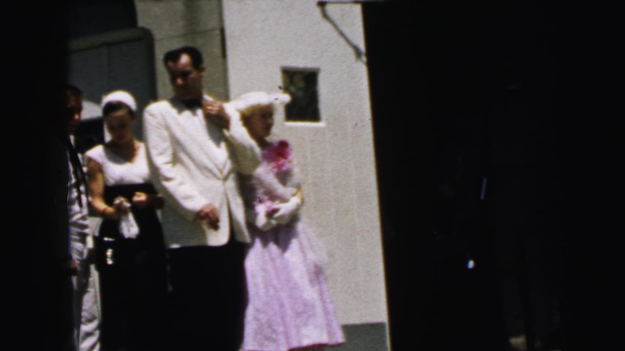 Wedding party members stand at the church entrance in Camden, with the groom in a white jacket and a woman in lavender near the doorway.