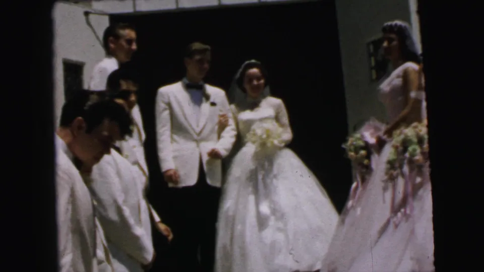 Camden wedding home-movie frame showing the couple, attendants, bouquets, and partial figures at the edge.