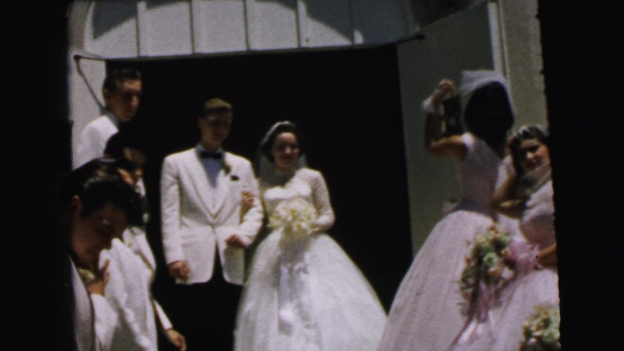 Bride and groom stand at a church doorway with attendants nearby.