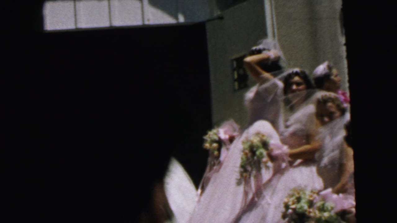 Pink-dressed bridesmaids gather near the church doorway holding bouquets.