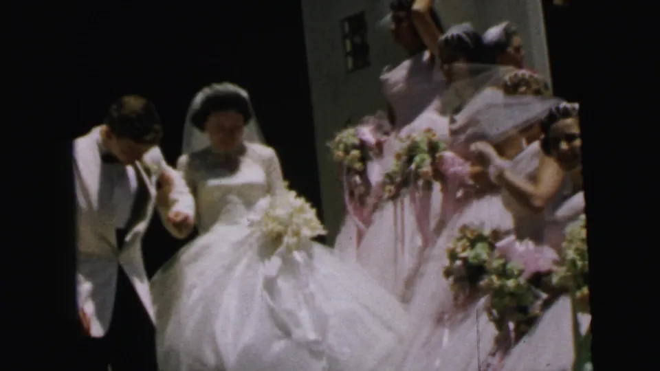 1964 Camden home-movie still showing the bride and groom moving forward as bridesmaids and guests crowd around with bouquets.