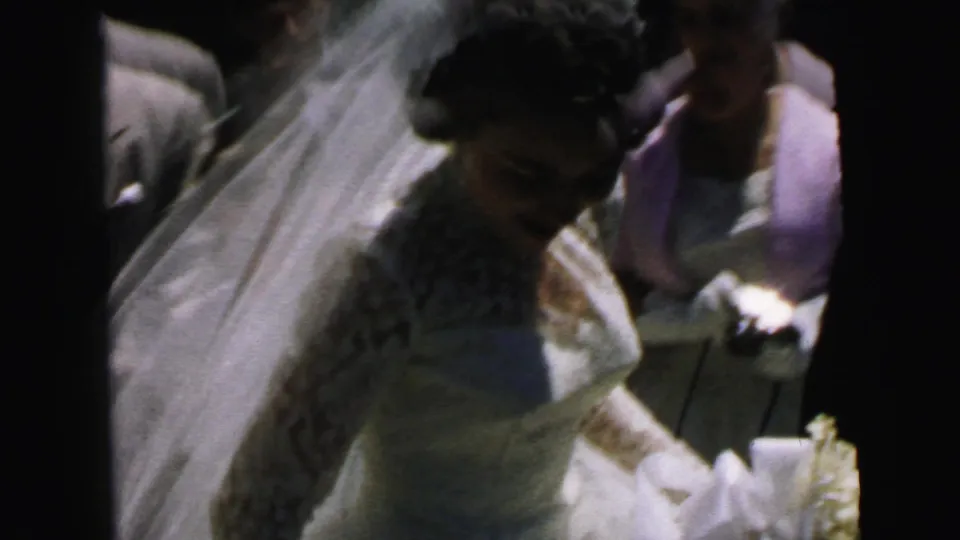 Bride in a white lace dress and veil appears beside guests during a 1964 Camden wedding departure.