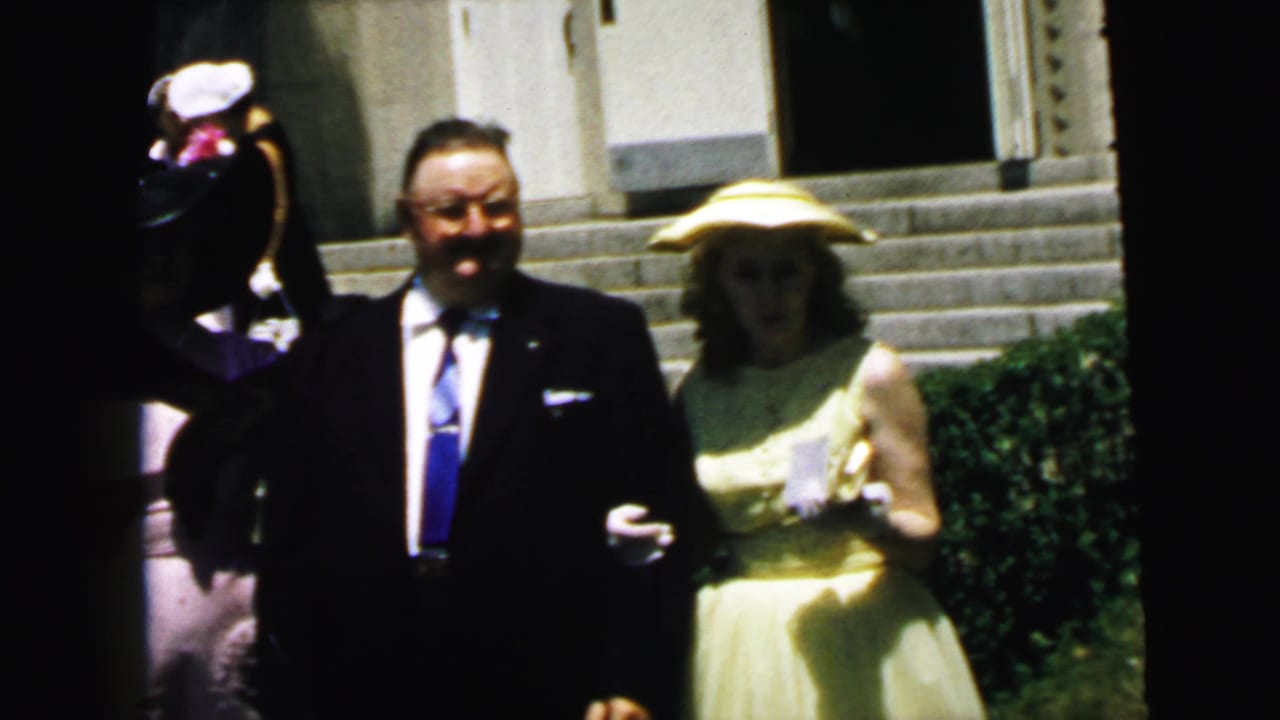 1964 Camden church exterior frame with formally dressed adults standing close together, including a woman in a yellow dress and broad hat.