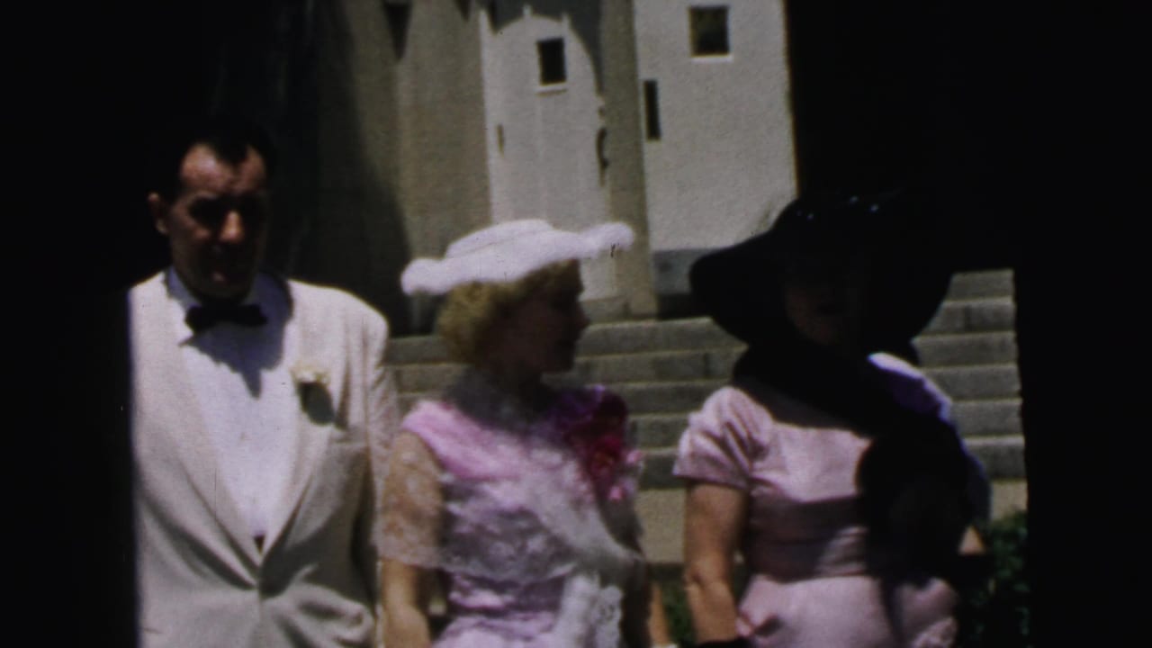 The 1964 Camden home movie shows a white-jacketed man, a woman in pink with white gloves, and another woman in a dark hat near stone steps.