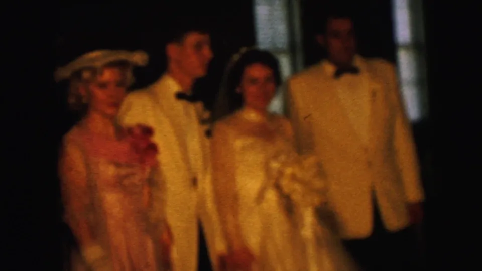 In this 1964 home-movie frame, the wedding party faces the camera, with the bride's veil and bouquet visible in warm 8mm light.