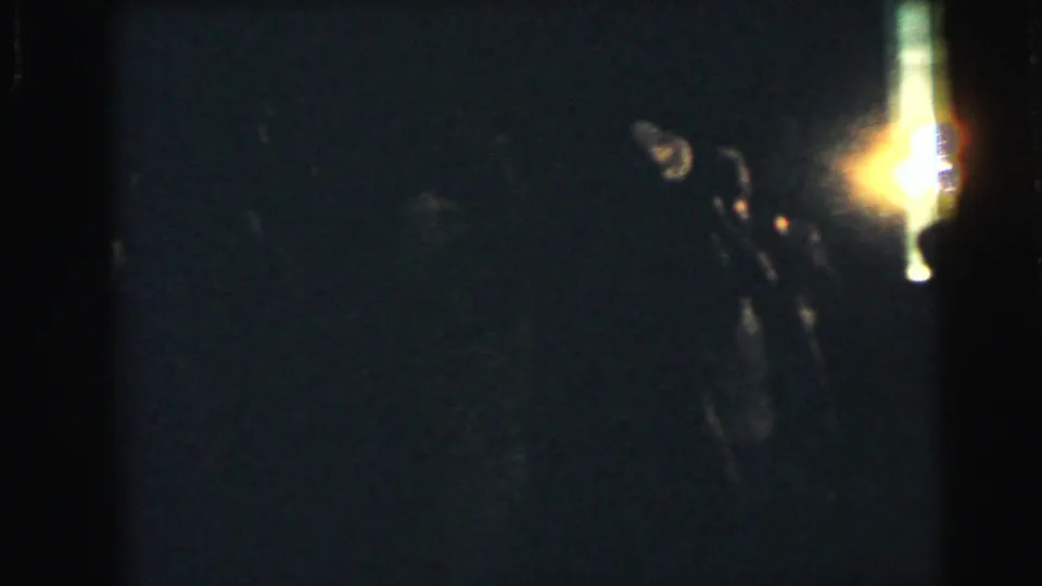 Dim 1964 home-movie frame with a bright light at the right edge, likely during a reception or dance transition.