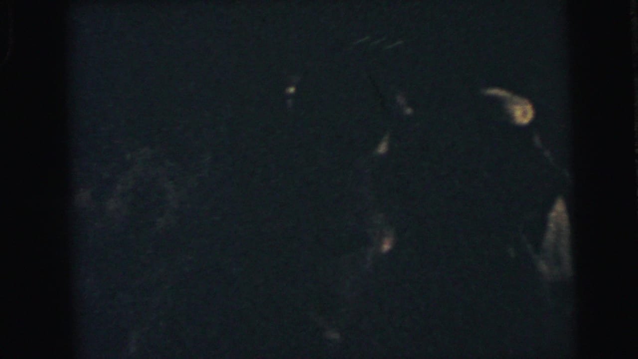 Dark 8mm frame with barely visible couples dancing in formal clothing.