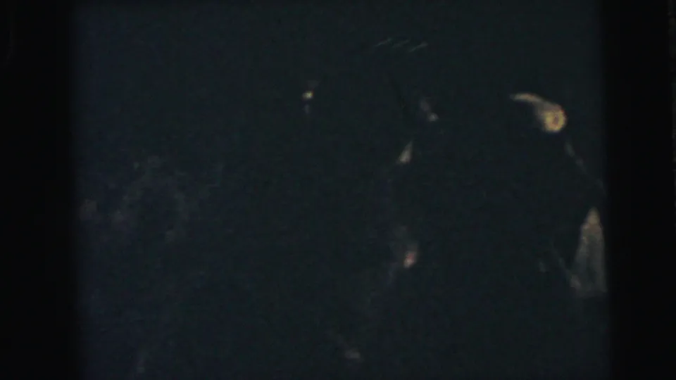 Low-light 1964 Camden home-movie frame showing shadowed couples dancing at an evening event.