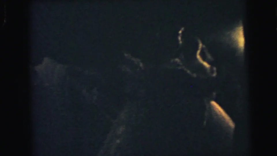 Grainy 8mm frame from Camden in 1964 with a formally dressed couple partly lit while dancing.