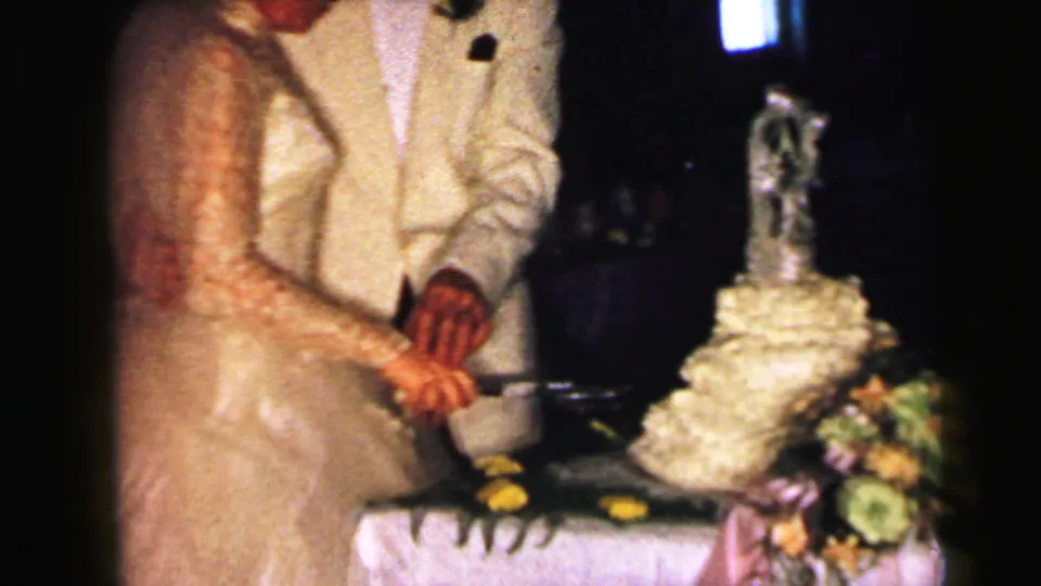 Bride in a lace gown and groom in a light jacket cut a tiered cake during the 1964 Camden wedding reception.