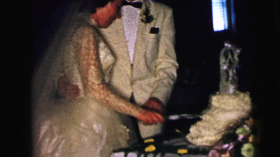 Close reception view of the bride and groom cutting the wedding cake, with flowers and a cake topper visible nearby.