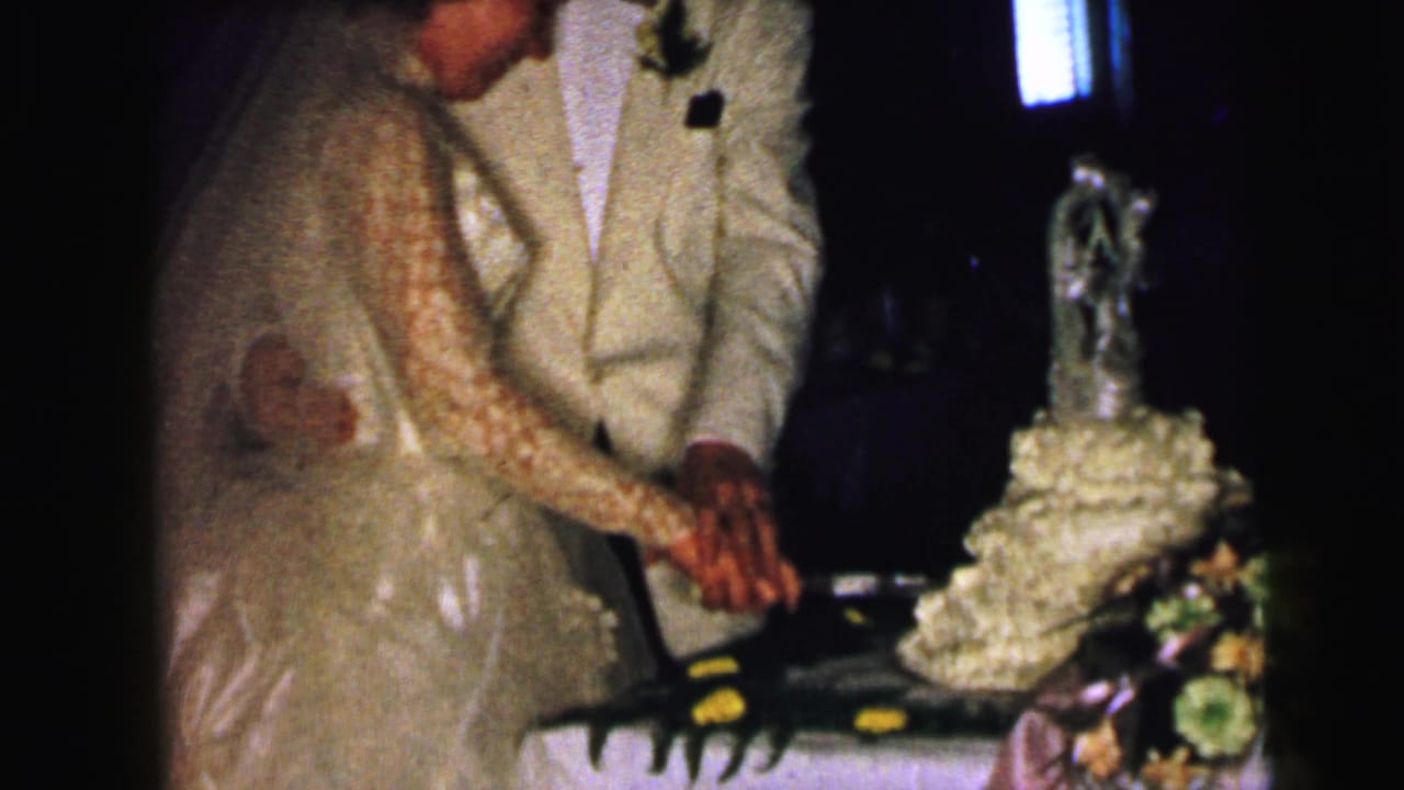 Bride and groom hold a knife together beside a tiered wedding cake.