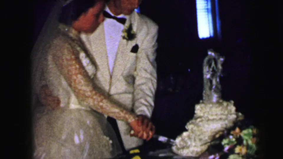 At the Camden wedding reception, the couple remains close at the cake table with flowers, a tiered cake, and a small topper visible.