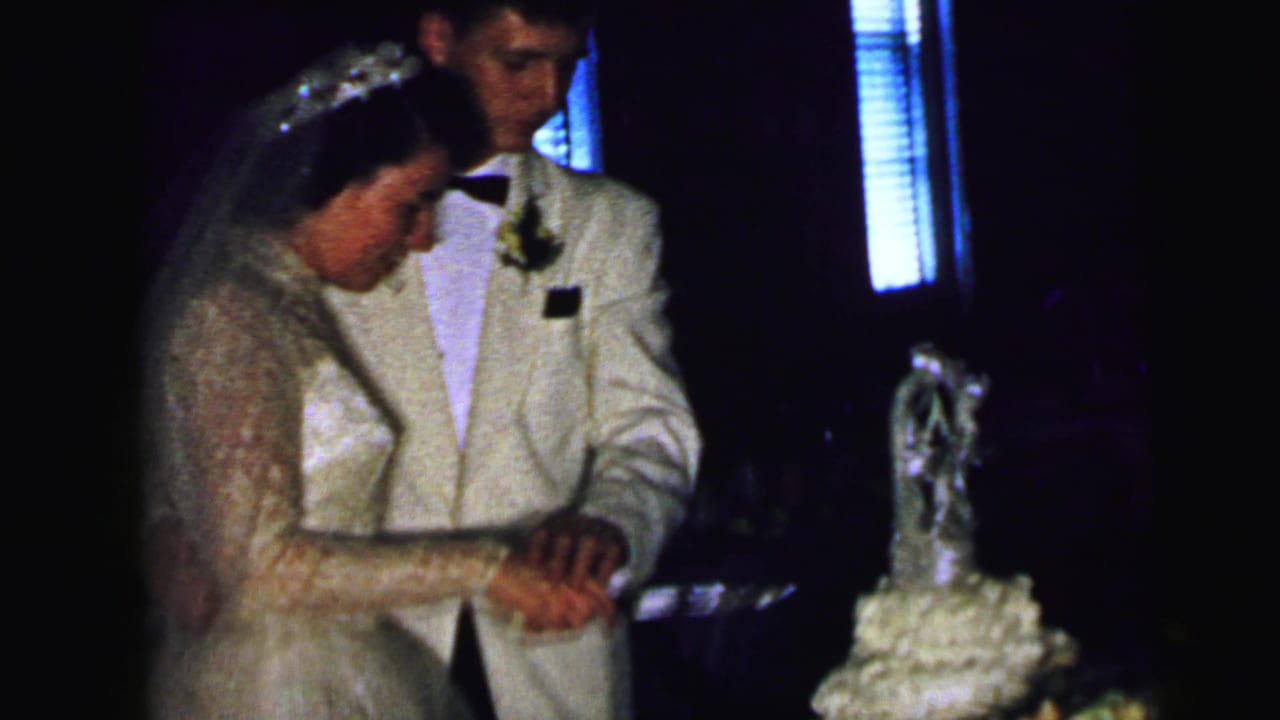 The bride and groom remain close together at the cake table, hands joined on the knife near the decorated wedding cake.