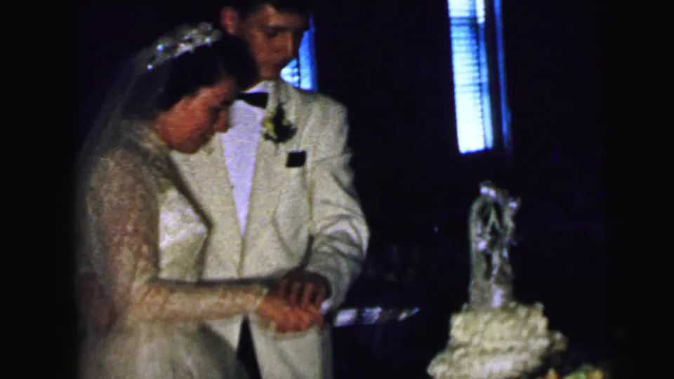 The bride and groom remain close together at the cake table, hands joined on the knife near the decorated wedding cake.