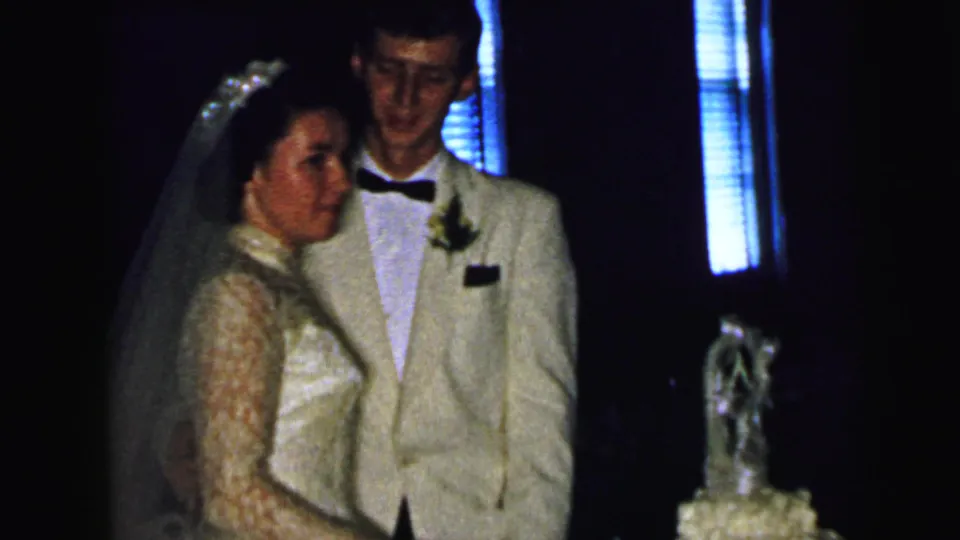 The 1964 Camden wedding couple stands near the cake, with the bride turned toward the camera and the groom partly behind her.