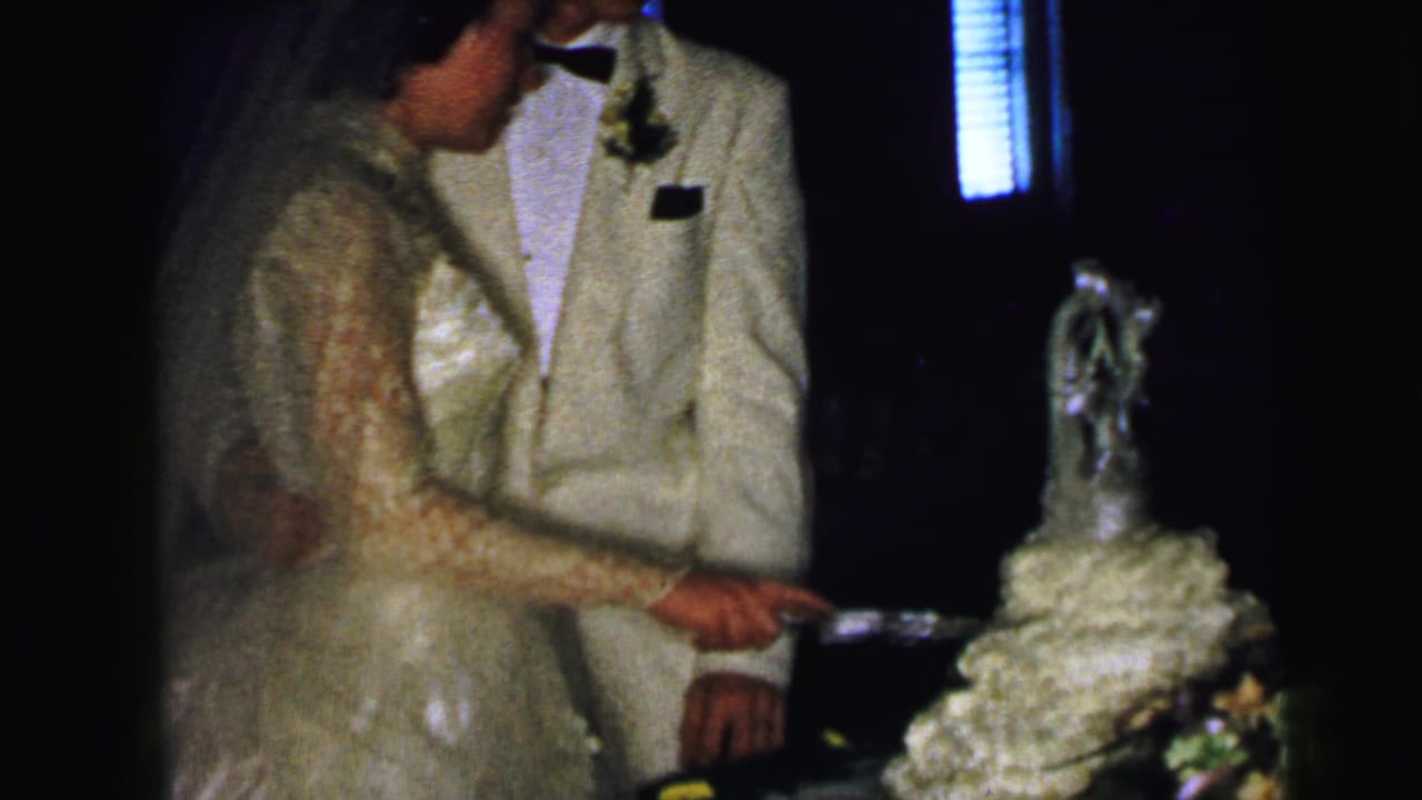 The bride and groom hold the cake knife together beside a tiered white cake in this 1964 Camden wedding reception shot.
