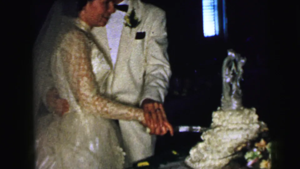 A close home-movie view shows the couple's hands joined on the knife as they begin cutting the wedding cake in Camden, 1964.