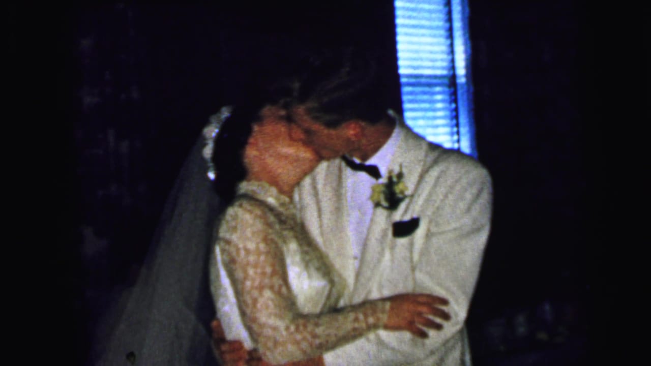 In 1964 Camden wedding footage, a bride in a veil and lace sleeves kisses a groom in a light tuxedo.
