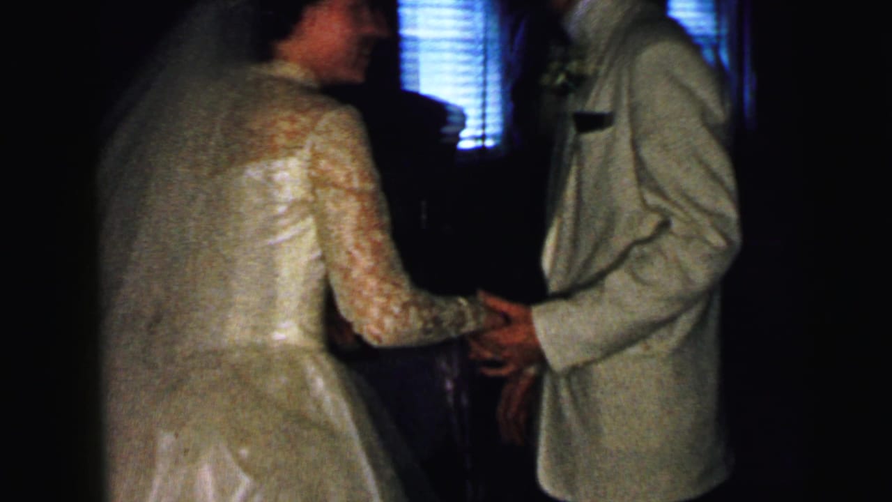 Bride and groom hold hands while dancing in a dim reception room.
