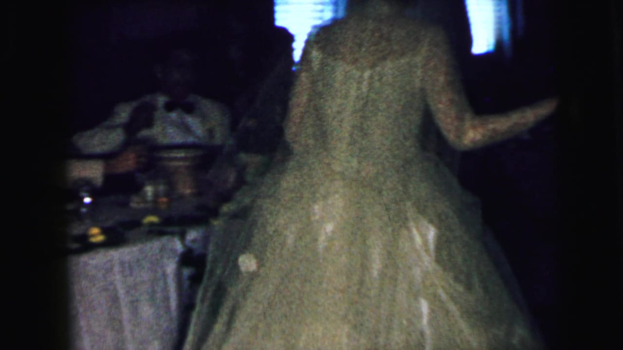 The bride in a long veil and lace wedding gown moves near a table during the Camden wedding reception footage.