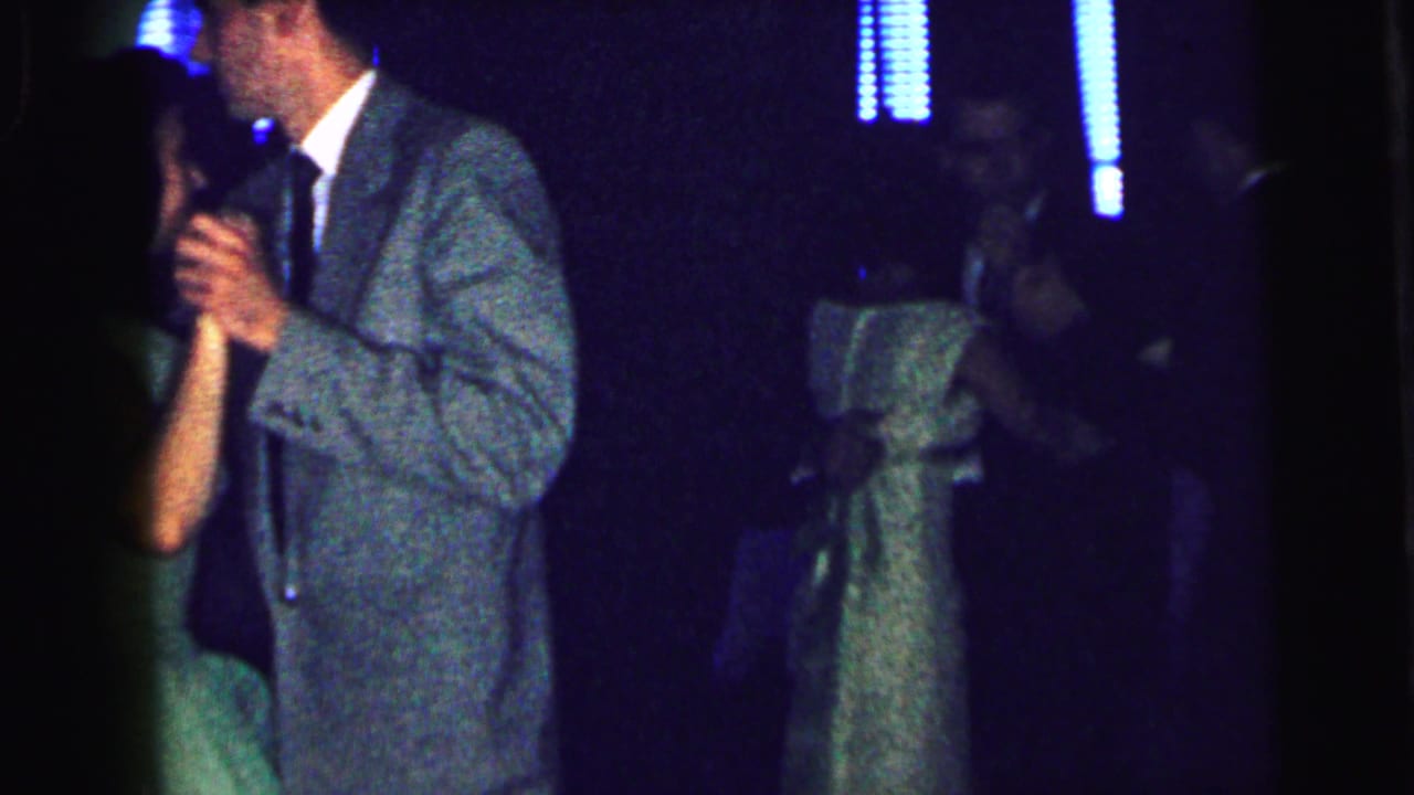 Young couple dancing closely in a dim room, with the girl in a pale green dress and the boy in a gray suit.