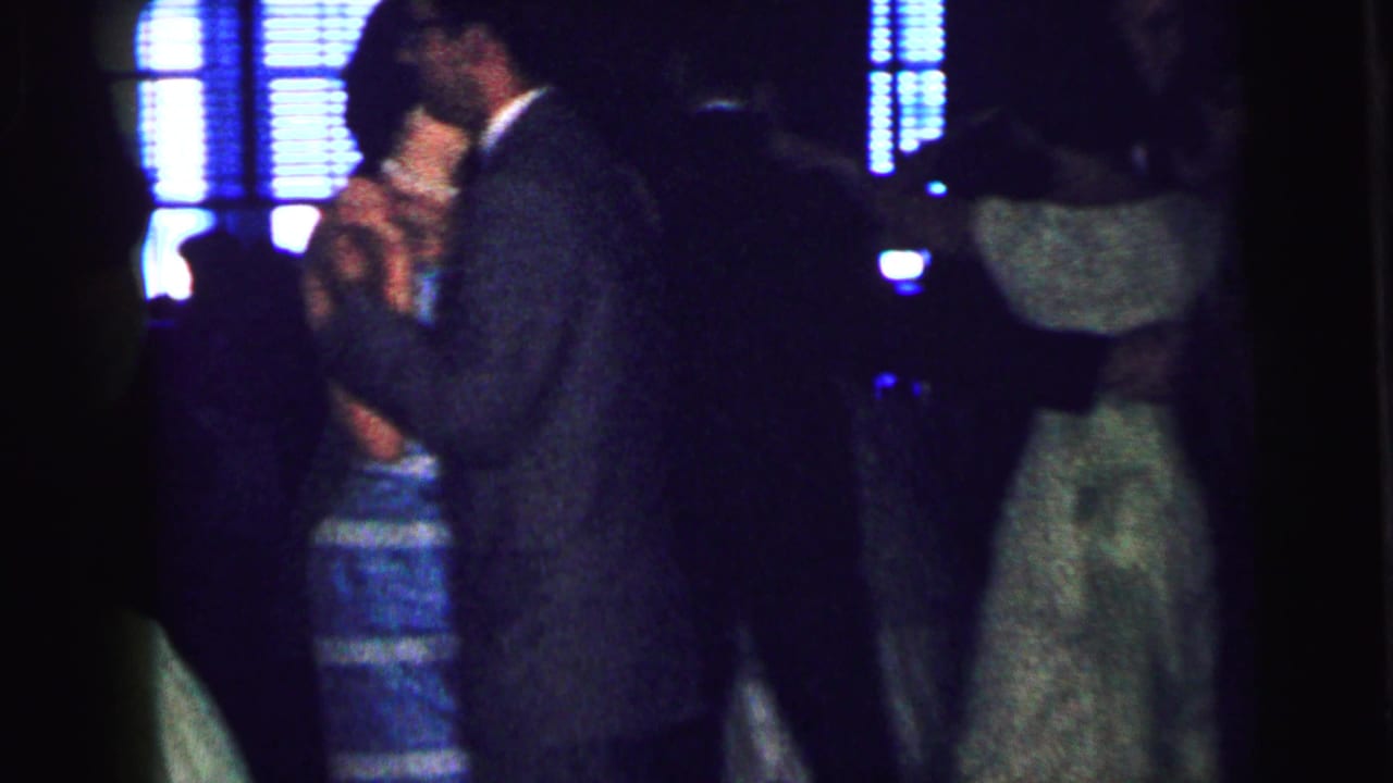 1964 Camden home-movie frame showing couples in suits and dresses dancing closely under dark blue lighting.