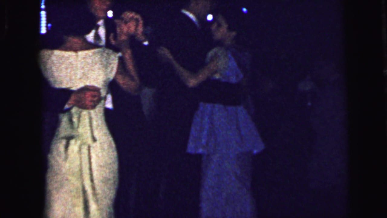 1964 Camden dance scene with a woman in a white dress and other couples moving in low light.